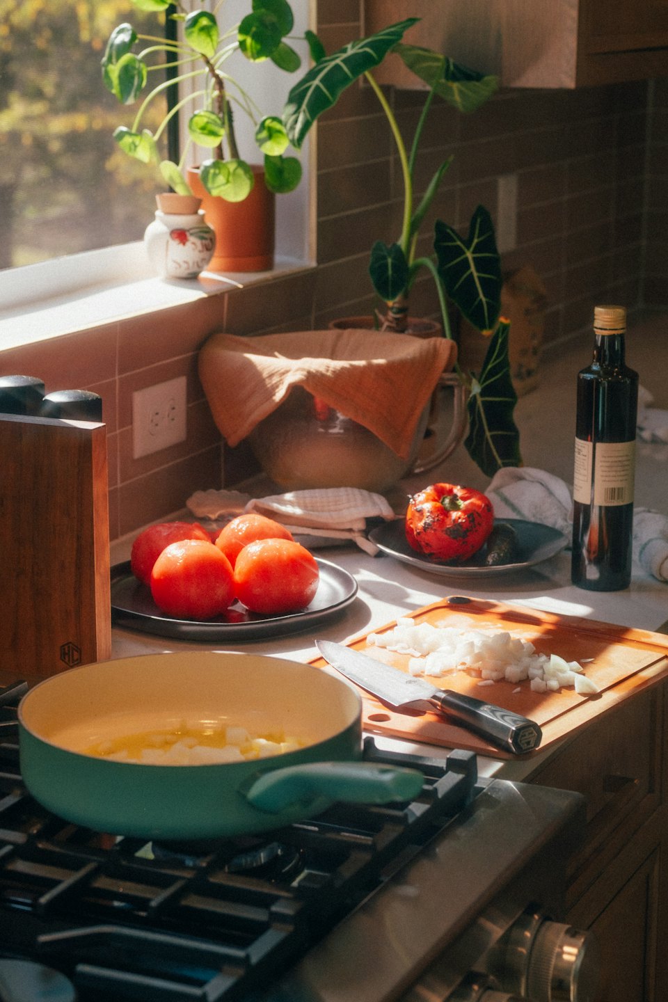 Green saucepan heats diced onions on a stovetop next to a cutting board.